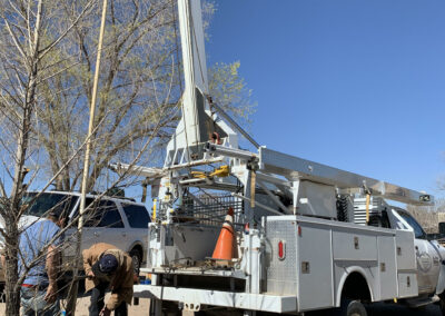 A crane truck is backed up to a well. Workers are inspecting a large pipe rising from the ground, surrounded by an old tire.