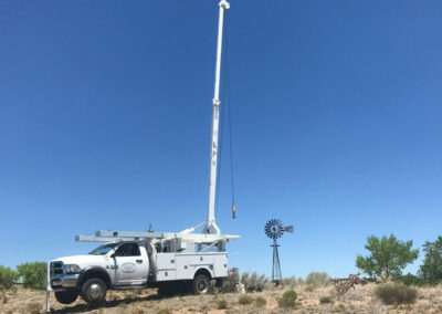A crane truck is parked in the New Mexico desert in front of a windmill.